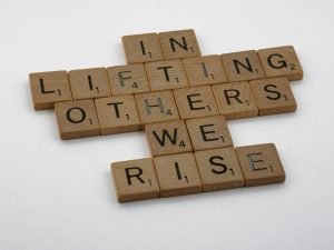 Wooden tiles spelling 'In lifting others, we rise', representing leadership and career development