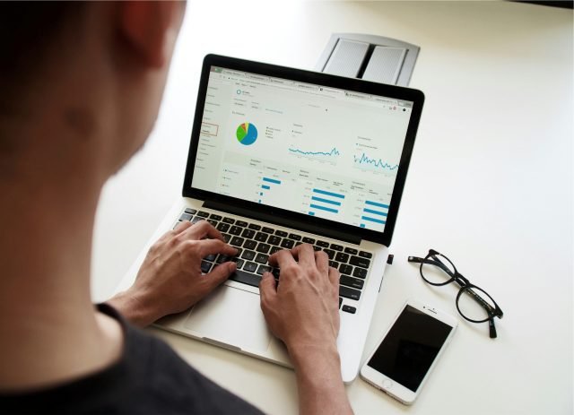 Person typing on a laptop while reviewing an analytics dashboard with charts