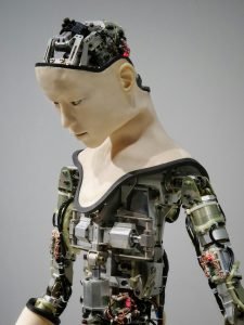 Close-up of a humanoid robot's exposed internal mechanics, head tilted, against a plain gray studio background