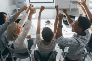 Diverse team of technology leaders around a table celebrating with raised hands