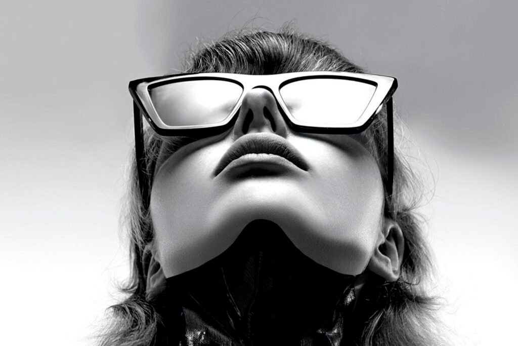 Black-and-white portrait of a person wearing bold sunglasses, looking up
