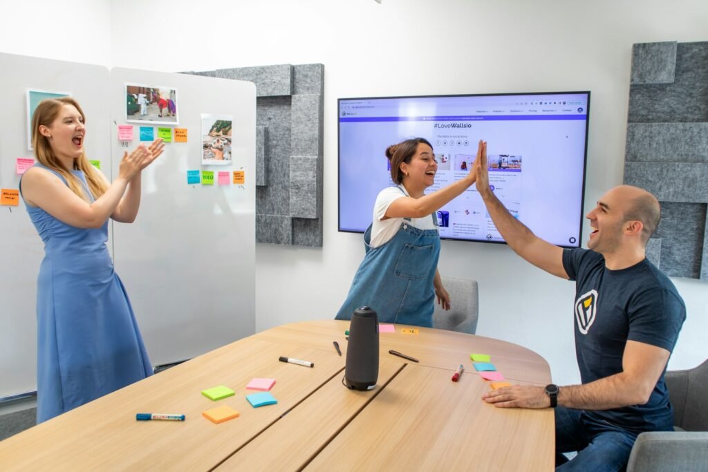 Three colleagues celebrating in a meeting room with a conference speaker device on the table