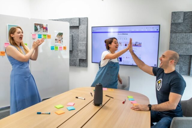Three colleagues celebrating in a meeting room with a conference speaker device on the table